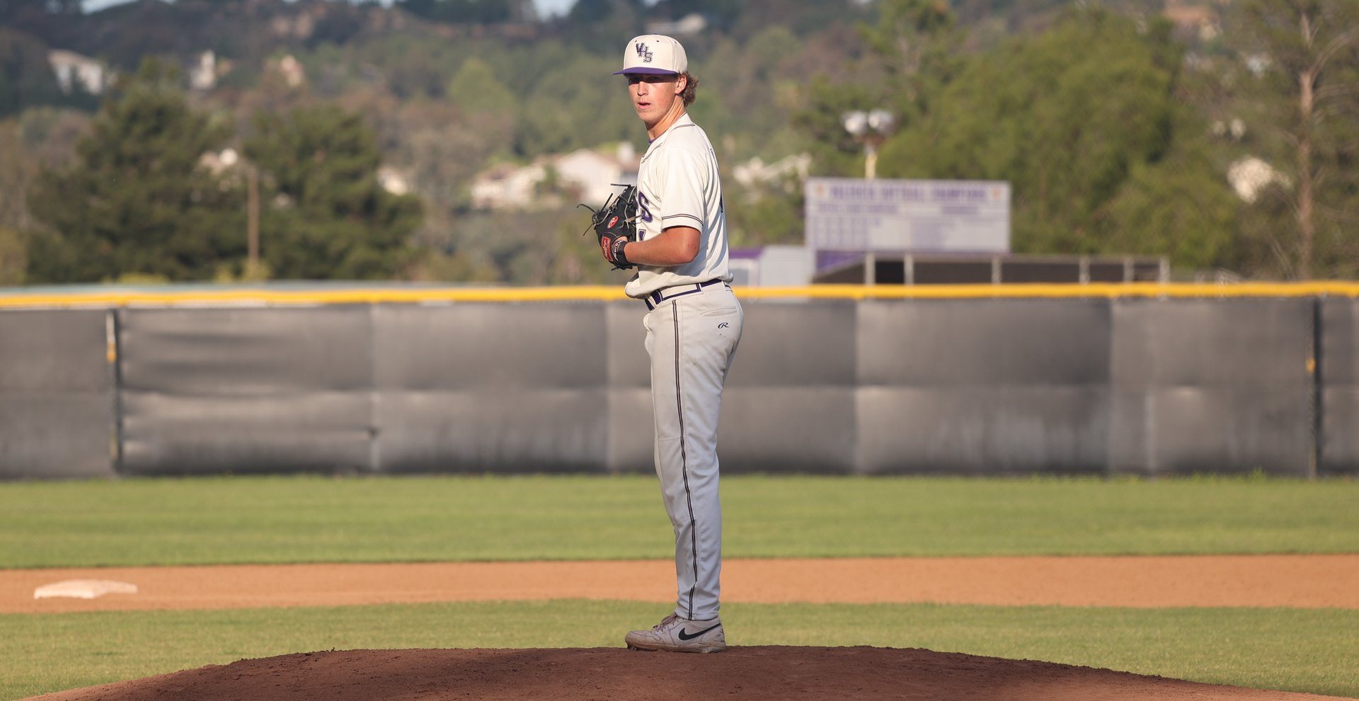 A Valencia pitcher set on the mound, the outfield wall and hillside behind him.