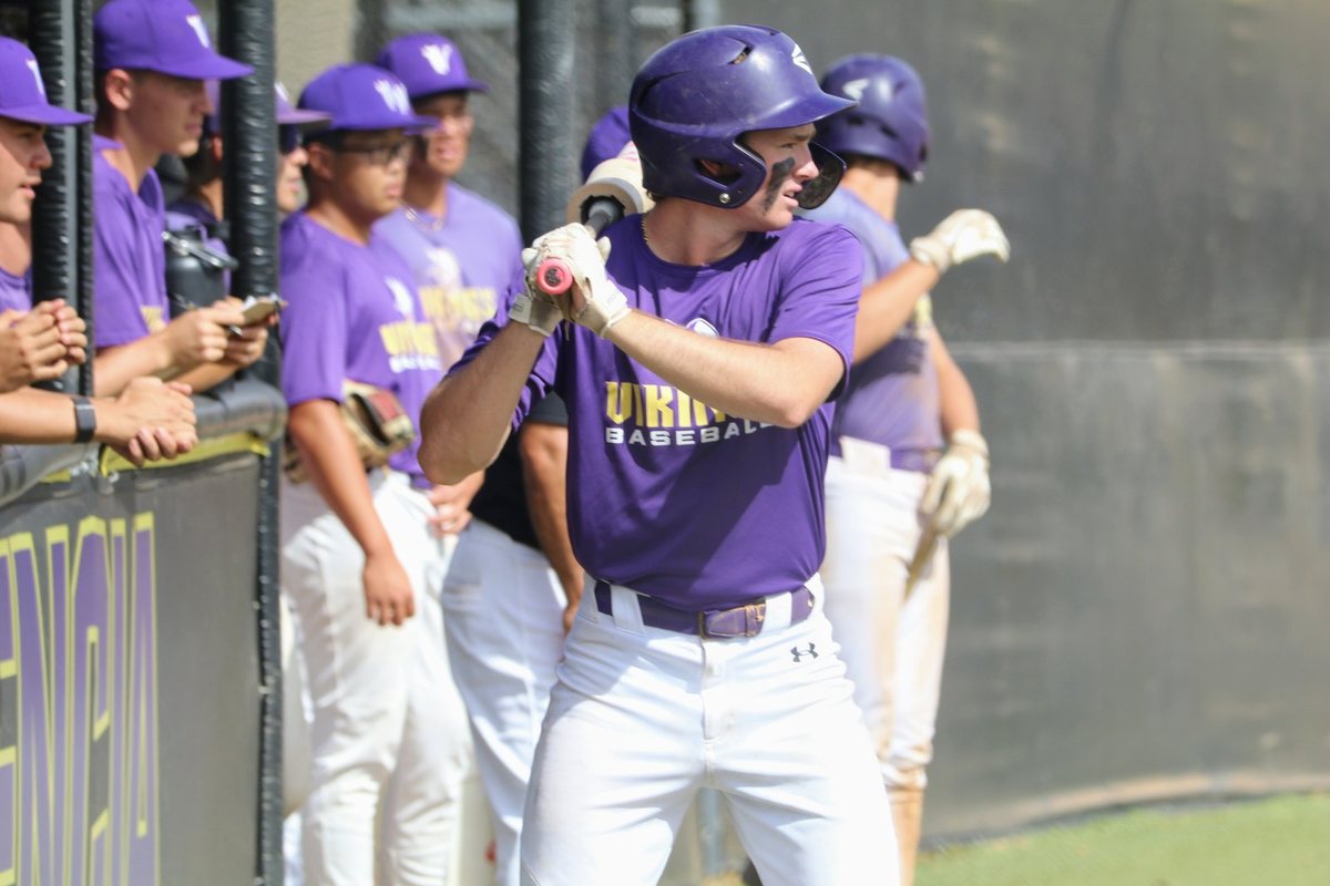 A Valencia hitter loading his swing in the on-deck circle, teammates watching from the dugout rail behind him.