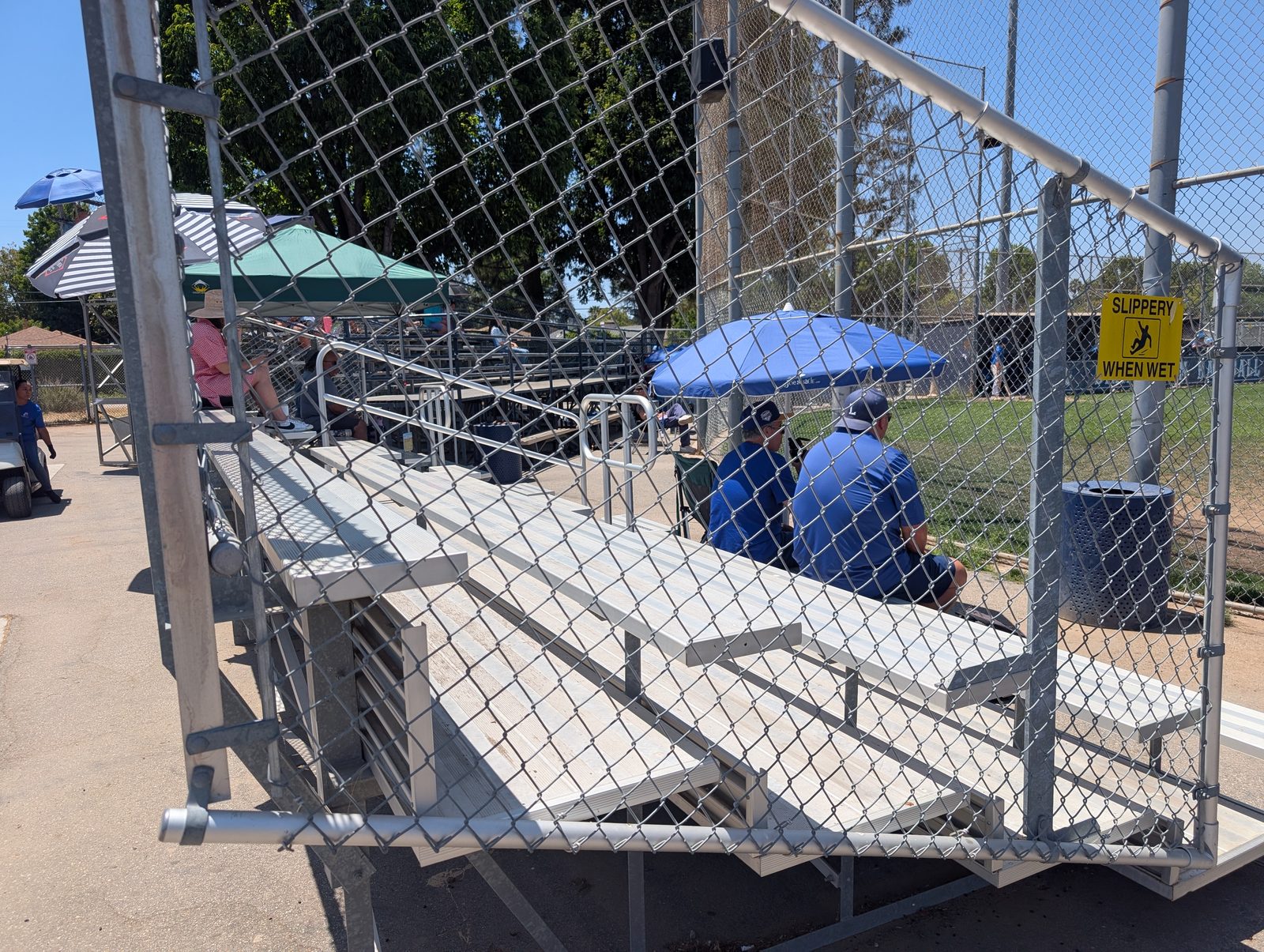 Inside the grandstand on a sunny day, parents using umbrellas for shade.