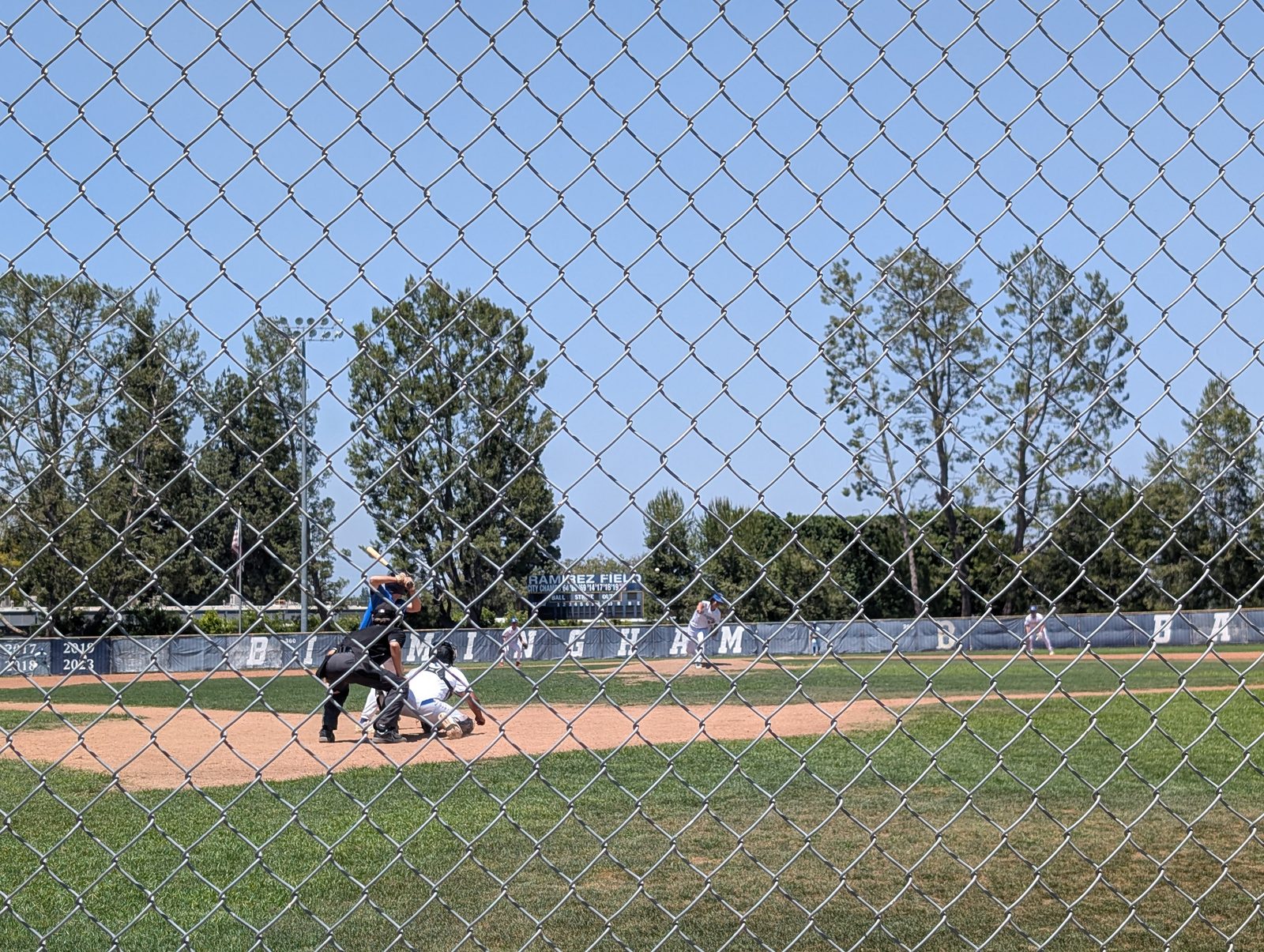 The clean sightline from behind home plate, through the backstop. Jaquez Field, with the 'Birmingham Baseball' wall.