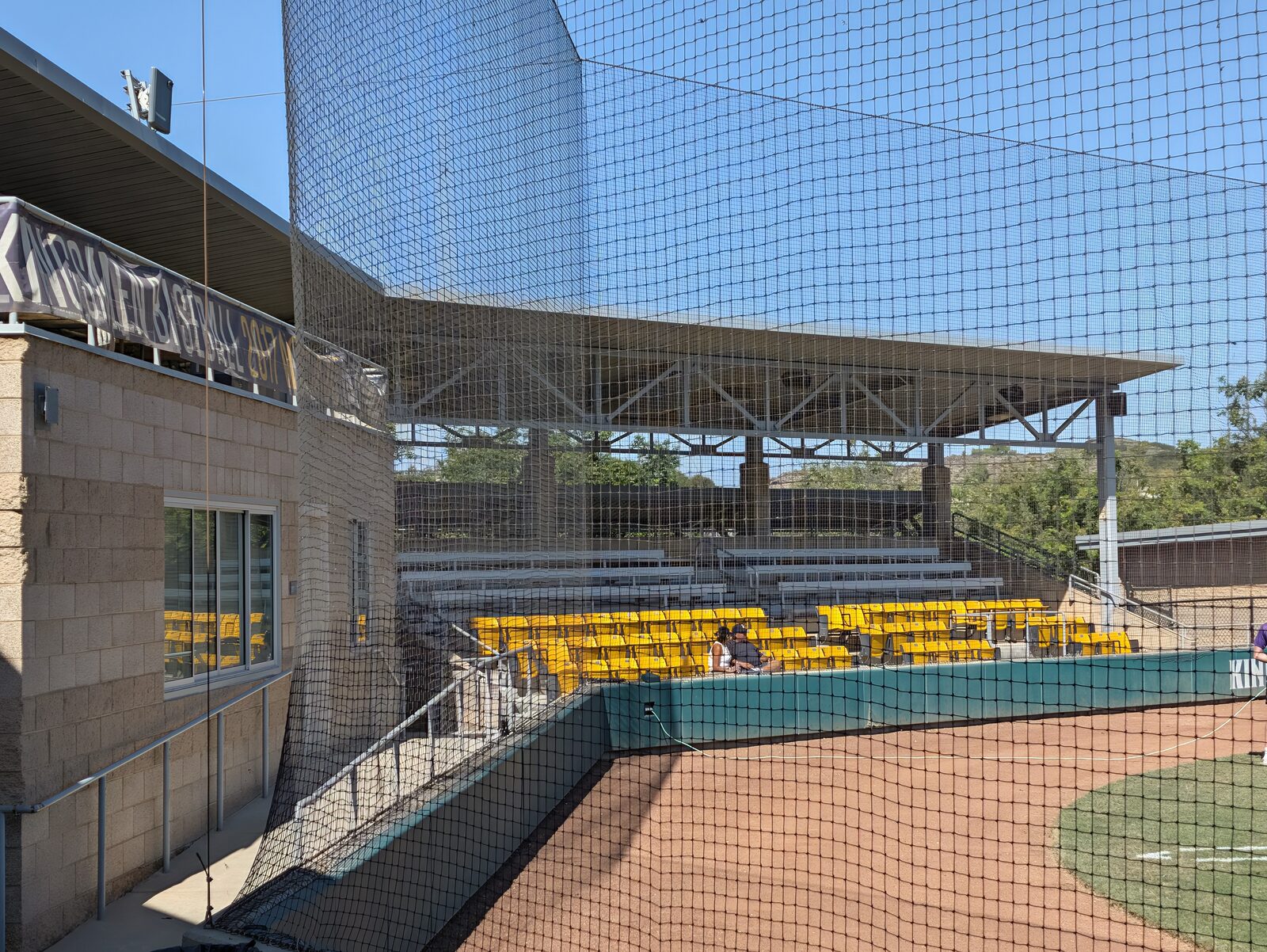 The press box and first-base-side seating: yellow chairbacks low, silver benches above. The benches have backs.