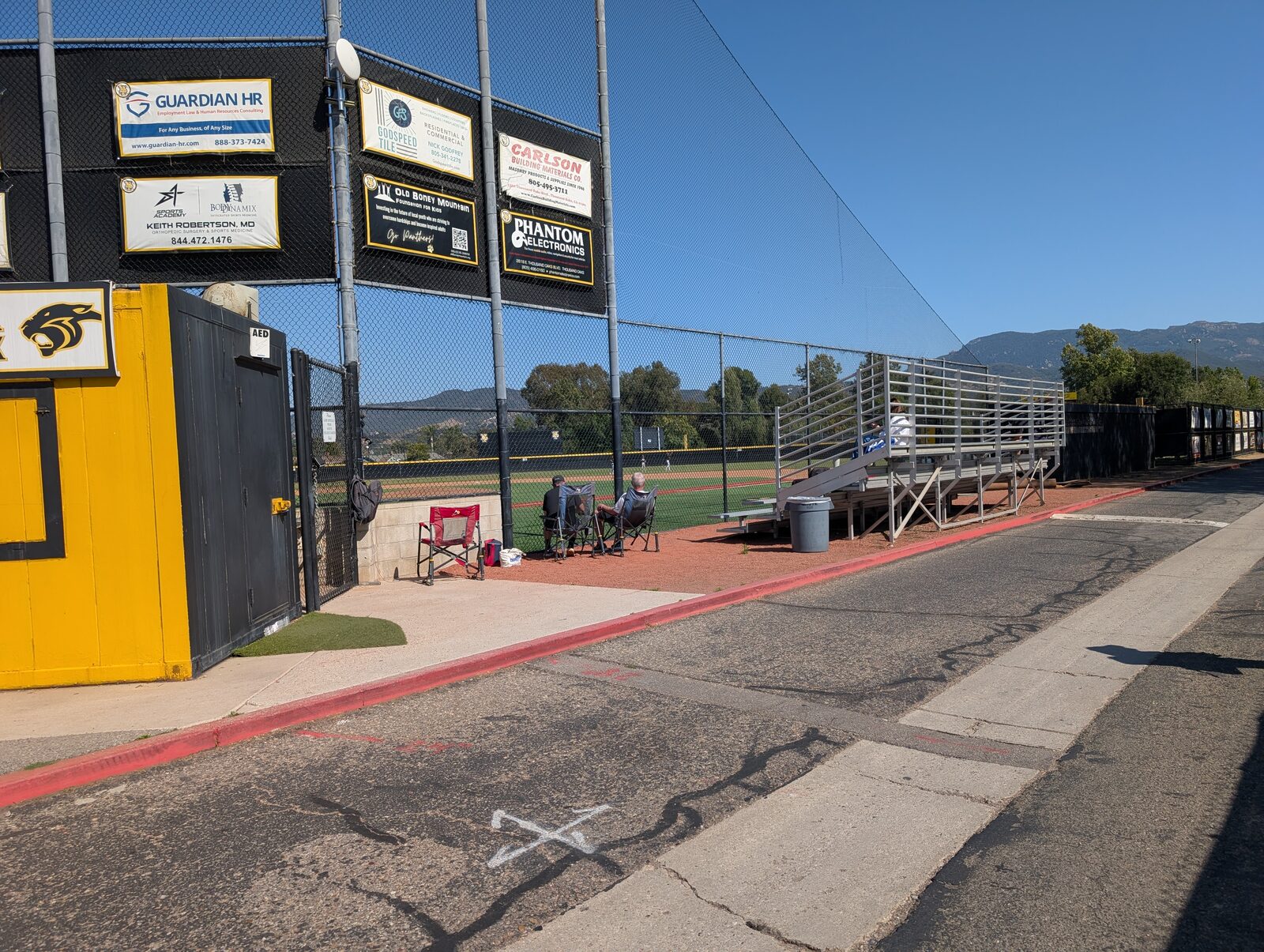 The entrance area, snack shack at left and a stretch of third-base-side bleachers at right. Compact sections, no canopy or shade.
