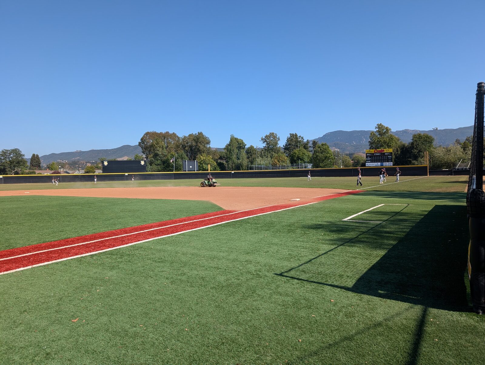 First-base-line view, players warming up. Scoreboard in right field, mountains beyond the fence.