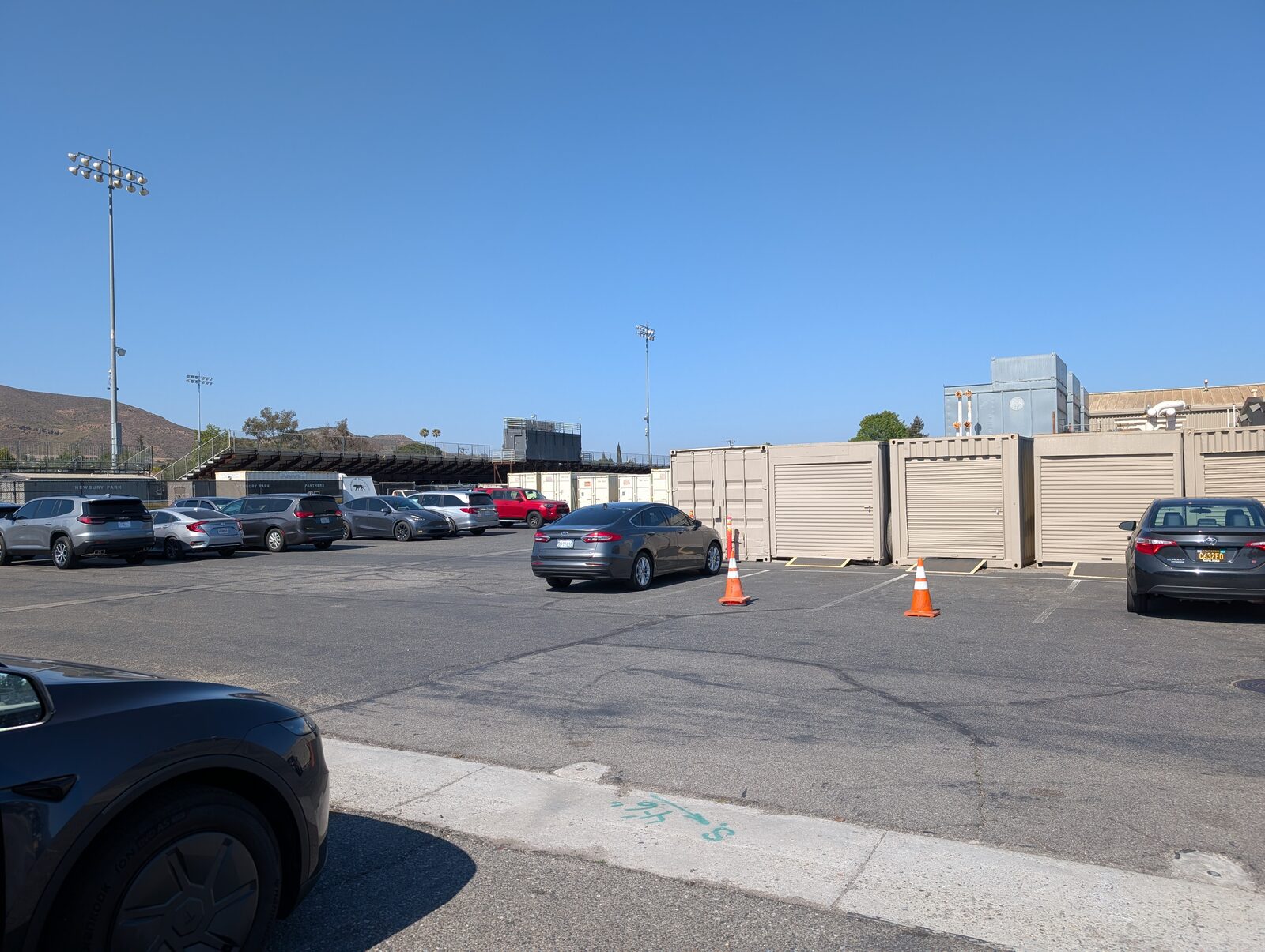 Wider view from the lot, third-base-side bleachers in the middle distance. Large lot, not crowded for a summer evening game.