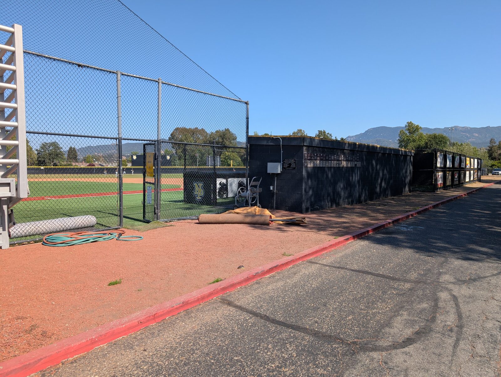 Third-base side: the home dugout and the batting cage. The field is artificial turf with a red dirt warning track.