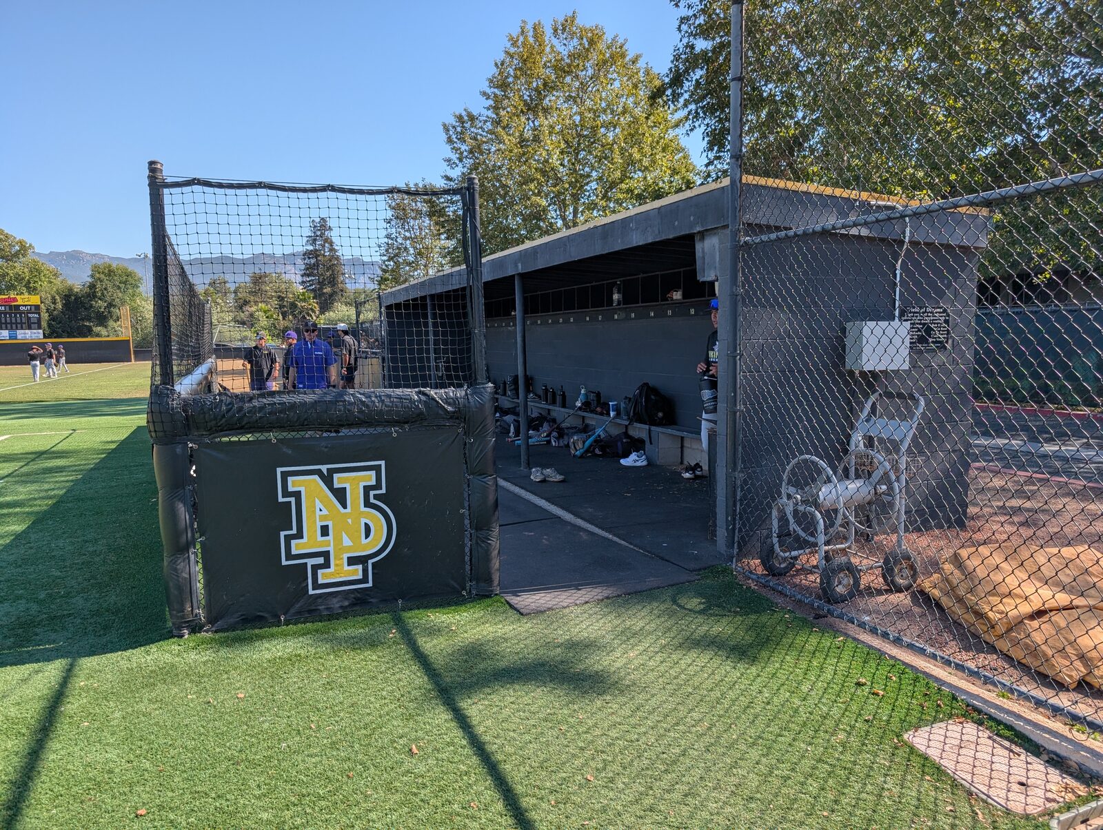 The visitor-side shelter, bench, and gear, with an NP Panthers wall pad. Likely the visitor batting tunnel.